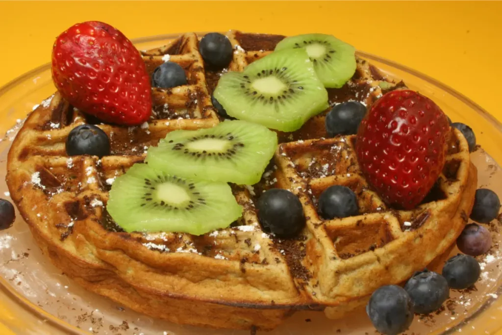 Stack of Kodiak waffles with blueberries and maple syrup on a wooden table with coffee.