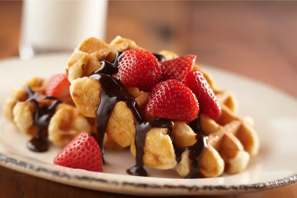 Stack of Kodiak waffles with blueberries and maple syrup on a wooden table with coffee.