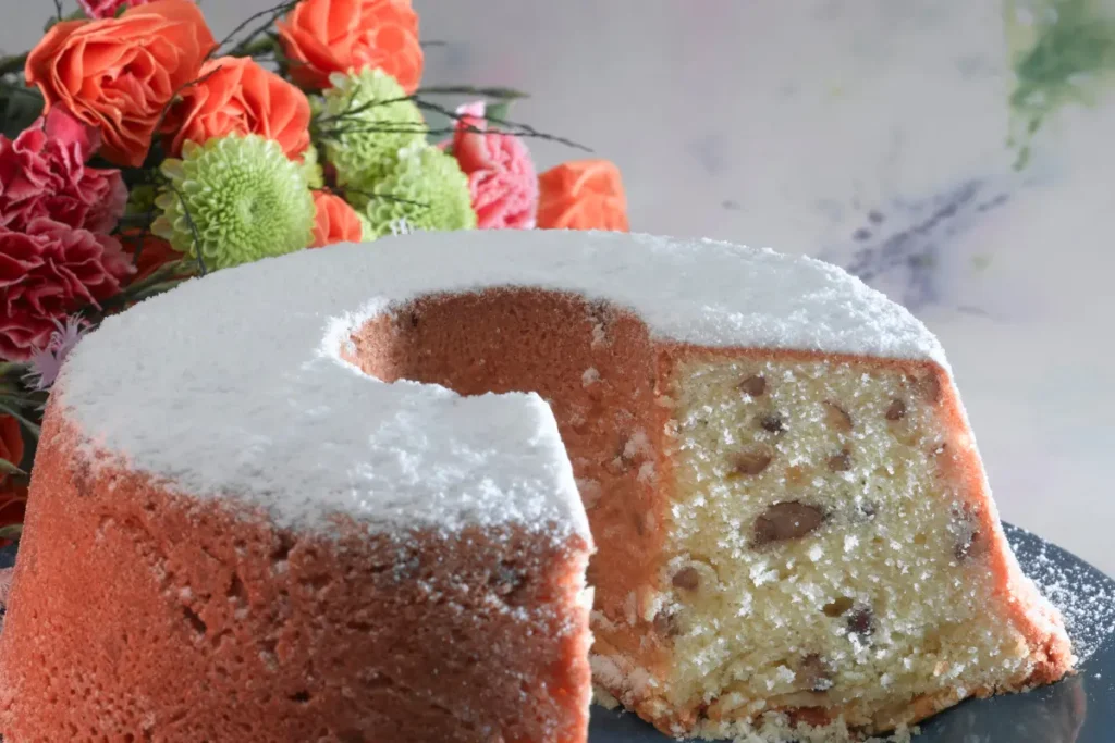 Freshly baked golden pound cake with raw ingredients like eggs, flour, sugar, and butter on a kitchen counter.