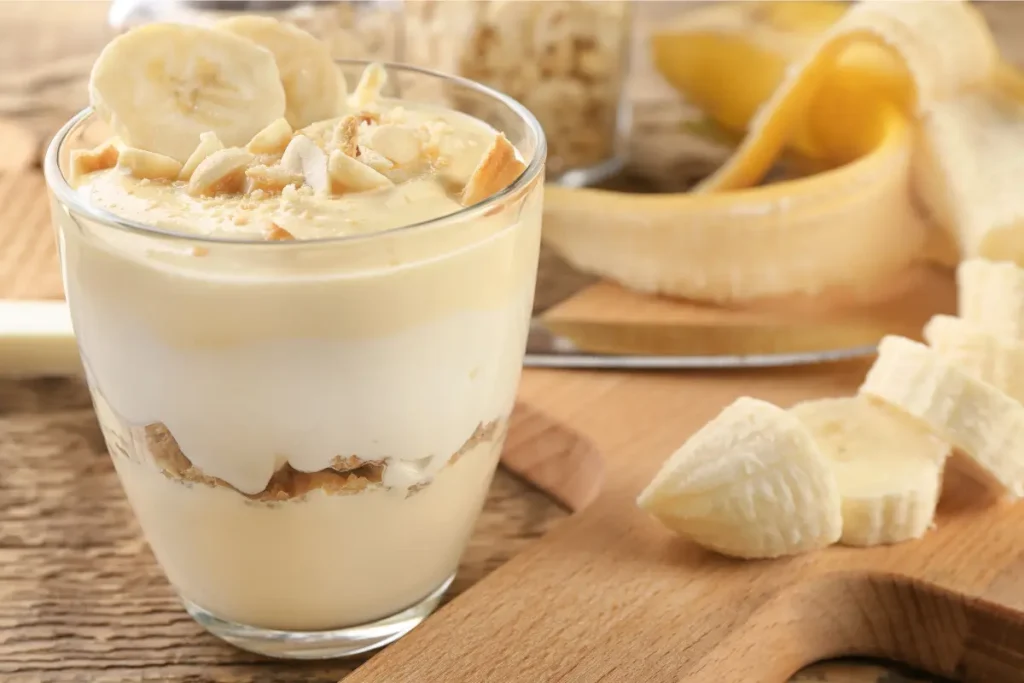 Fresh yellow banana and brown-spotted banana on a wooden surface with a bowl of lemon juice and a lemon half, demonstrating methods to prevent banana browning.