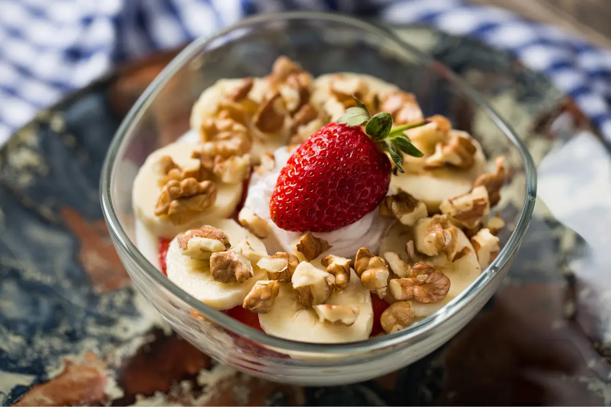 Bowl of Strawberry Banana Pudding with fresh slices of strawberries and bananas, topped with whipped cream and garnished with a strawberry slice and a mint leaf.