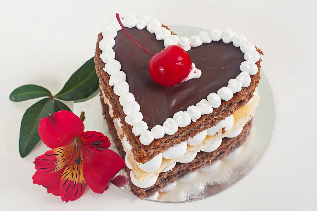 Decorated heart-shaped cake on white stand with icing roses, ready for serving.