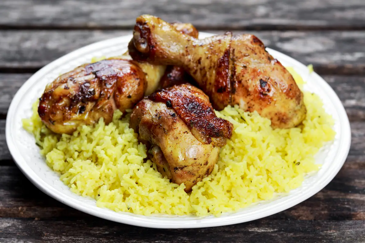 Steaming plate of chicken and yellow rice with cilantro and lemon on a wooden table.