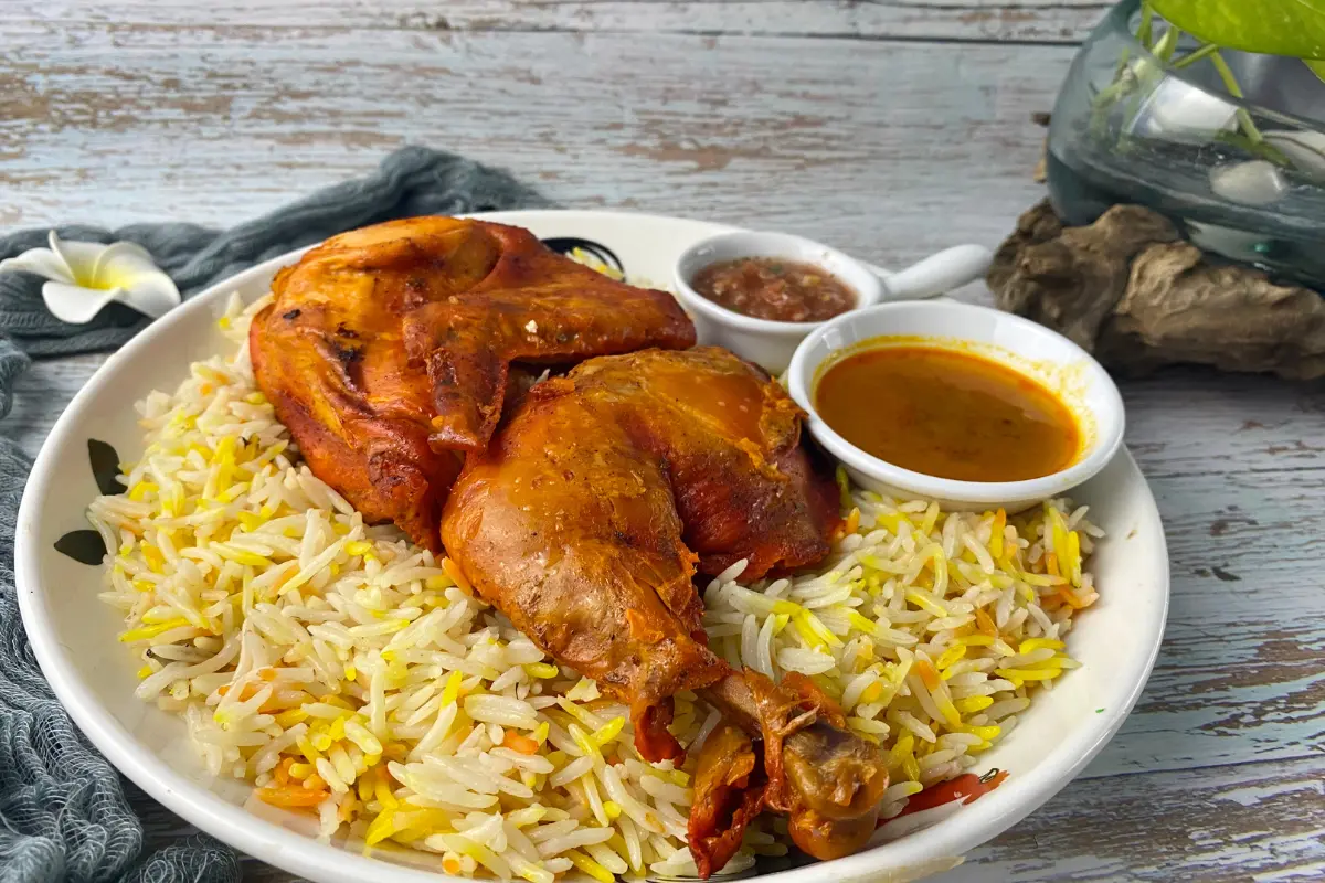 Steaming plate of chicken and yellow rice with cilantro and lemon on a wooden table.