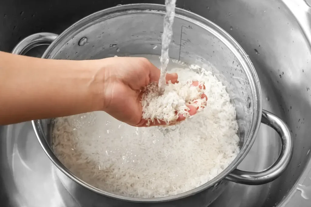 Washing yellow rice in a sieve under running water to remove excess starch and impurities.