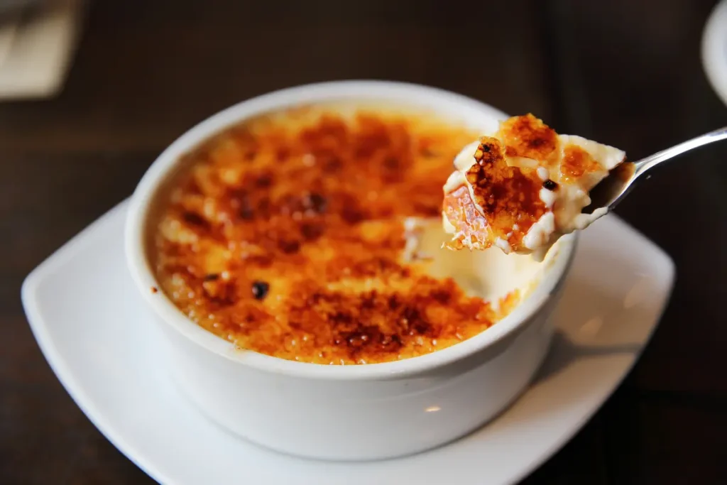 Perfectly caramelized crème brûlée with kitchen torch and vanilla pods in the background, showcasing the ideal texture and color of this classic dessert.