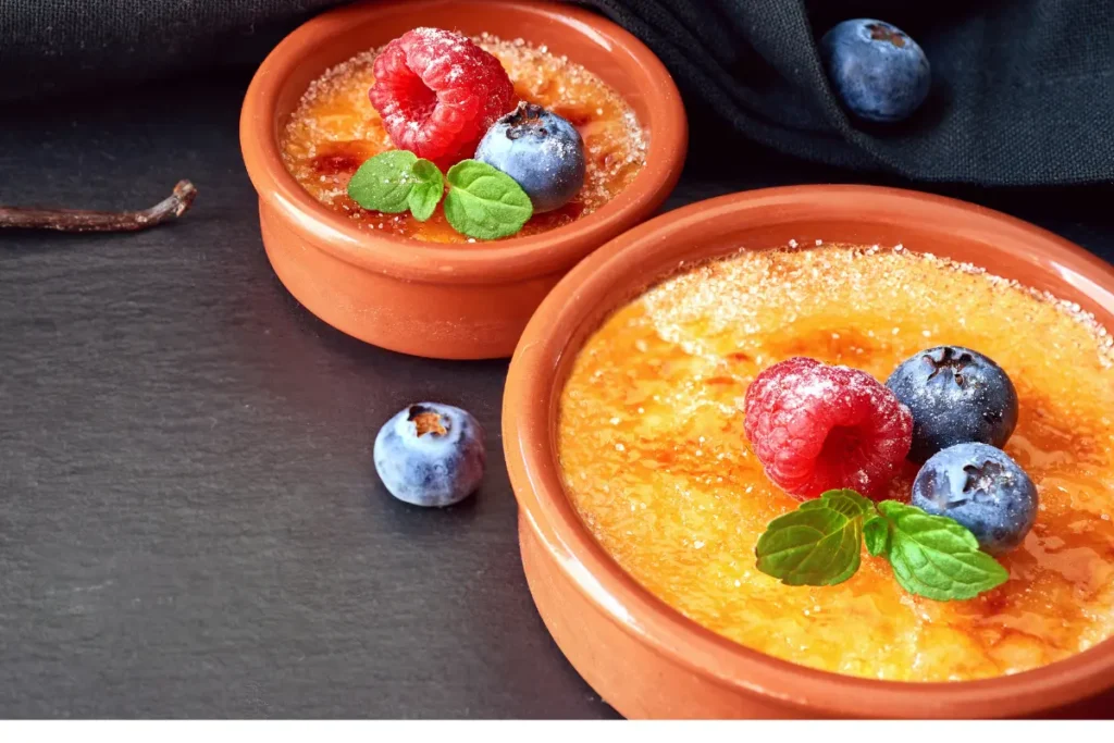 Perfectly caramelized crème brûlée in a ramekin with a spoon on a wooden table.