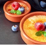 Perfectly caramelized crème brûlée in a ramekin with a spoon on a wooden table.