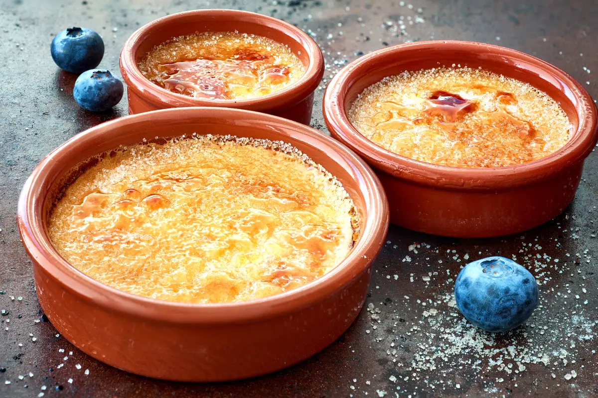 Perfectly caramelized crème brûlée in a ramekin with a spoon on a wooden table.